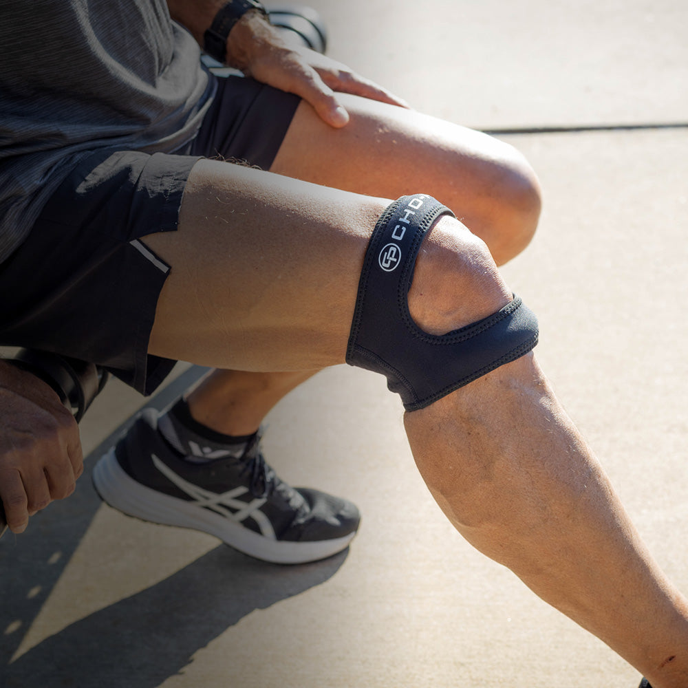 Person stretching outdoors while wearing the Cho-Pat Dual Action Lite Knee Strap on the knee.