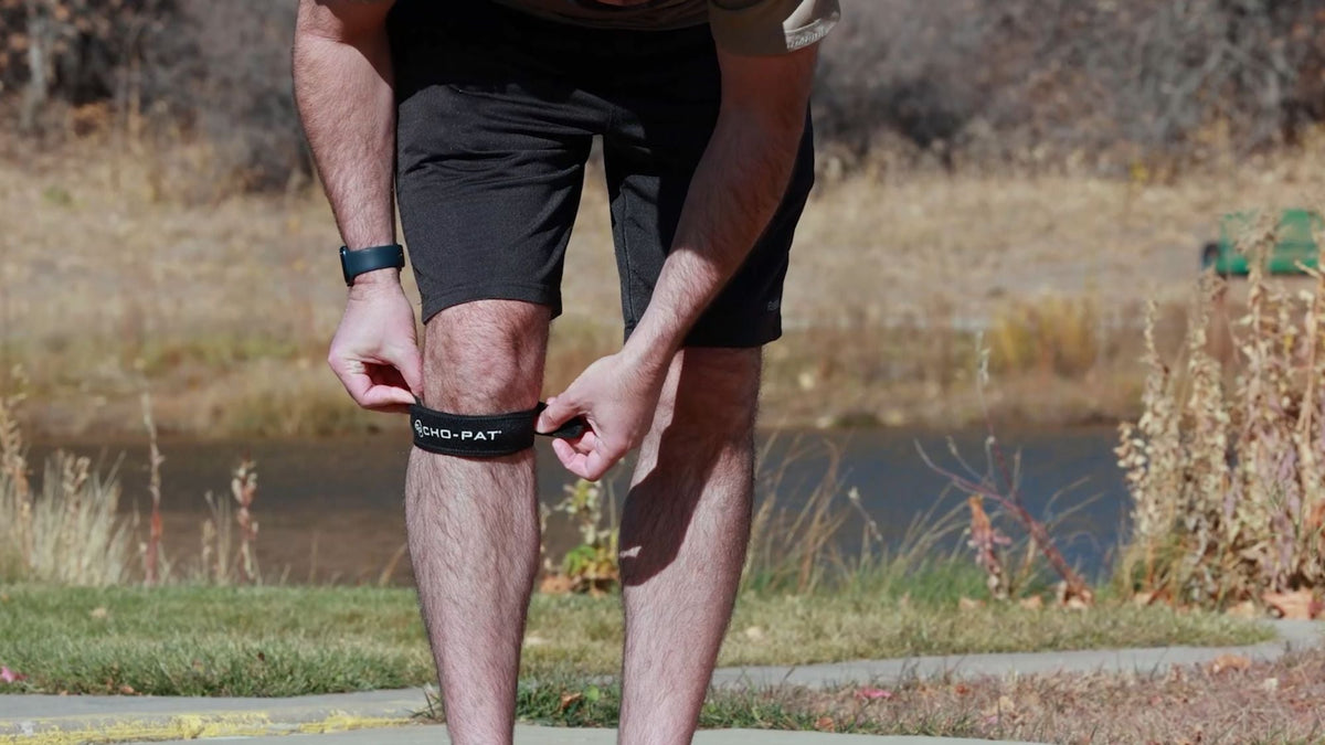 Man adjusting a Cho-Pat Patella Knee Strap below the kneecap before outdoor physical activity.