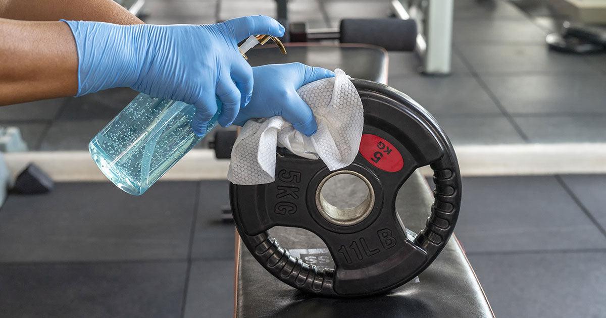 Gym staff disinfecting weight plate in the gym